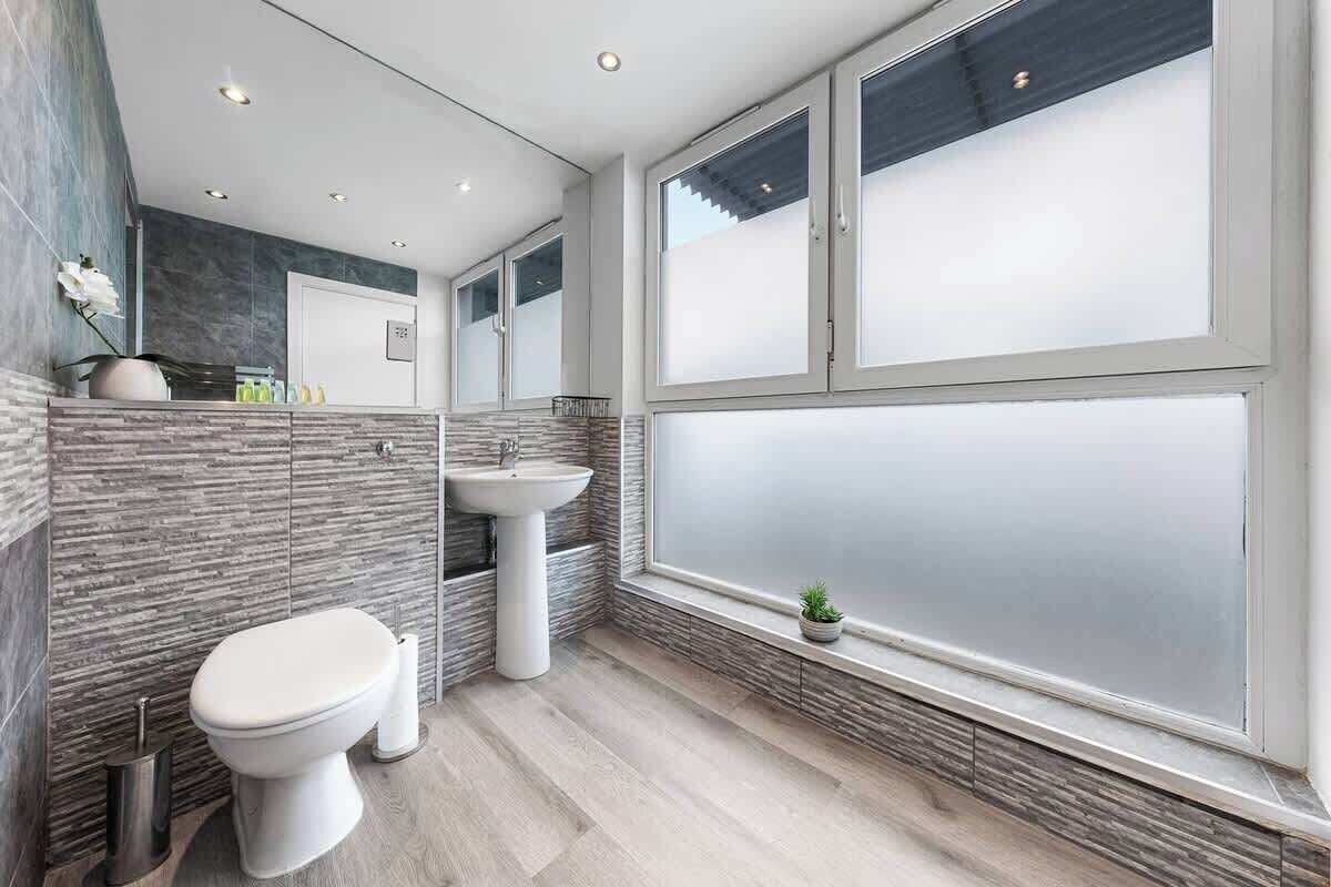 A modern bathroom with a toilet, sink, and large windows.