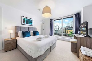 Quarto de hotel moderno com uma cama grande, uma mesa de cabeceira, uma televisão e vista da cidade através de uma janela ampla.