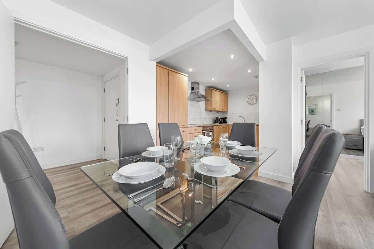 Un comedor moderno con una mesa de vidrio, sillas negras y una cocina al fondo.