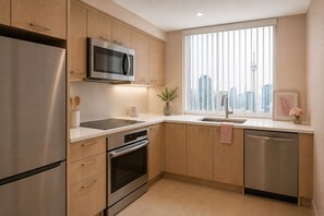 Eine moderne Küche mit Edelstahlgeräten, Holzschränken, einer eingebauten Mikrowelle und einem Fenster mit Blick auf die Stadt.