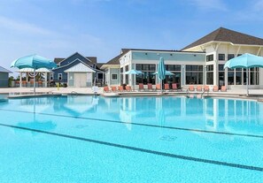 Una piscina con sillones de descanso y sombrillas, un edificio con ventanales grandes y un cielo despejado.
