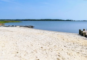 A sandy beach with a wooden dock extending into calm water, surrounded by a forested area.