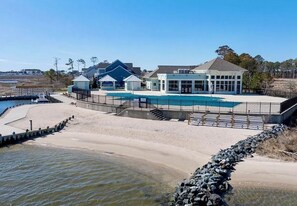Una propiedad frente a la playa con piscina, un patio cubierto y un edificio con amplios ventanales.