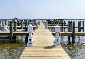 Un muelle de madera que conduce a un embarcadero con barcos amarrados, bollards blancos y un cielo despejado.