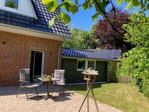 Ein Ziegelhaus mit Terrasse, kleiner Veranda und Garten.
