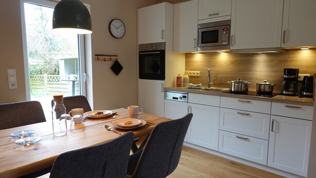 Una cocina moderna con armarios blancos, un microondas y un comedor con una mesa para dos.