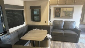 A compact RV interior with a kitchenette, a seating area with a table, and a sofa. - 1 bedroom and 3 bunk bed for rent in GIMLI sandy hook (Sandy Hook)
