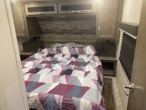 Habitació compacta amb un llit, un reposacapses de fusta i armaris de paret.