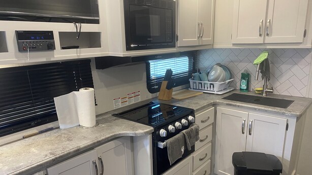 A kitchen with white cabinets, a black stove, a microwave, and a sink. - 1 bedroom and 3 bunk bed for rent in GIMLI sandy hook (Sandy Hook)