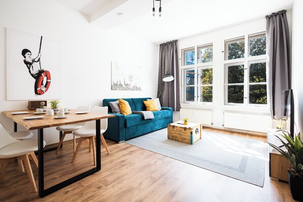 Una sala moderna con una mesa de comedor de madera, un sofá azul y un ventanal con cortinas.