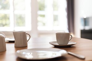 Une table avec une tasse blanche, une soucoupe et une assiette, avec une fenêtre en arrière-plan.