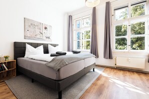 Un dormitorio moderno con una cama grande, una mesita de noche de madera, un radiador y una ventana con cortinas.