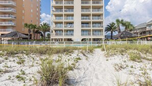 Un hôtel situé en bord de mer, avec un bâtiment principal, une plage de sable et des palmiers.