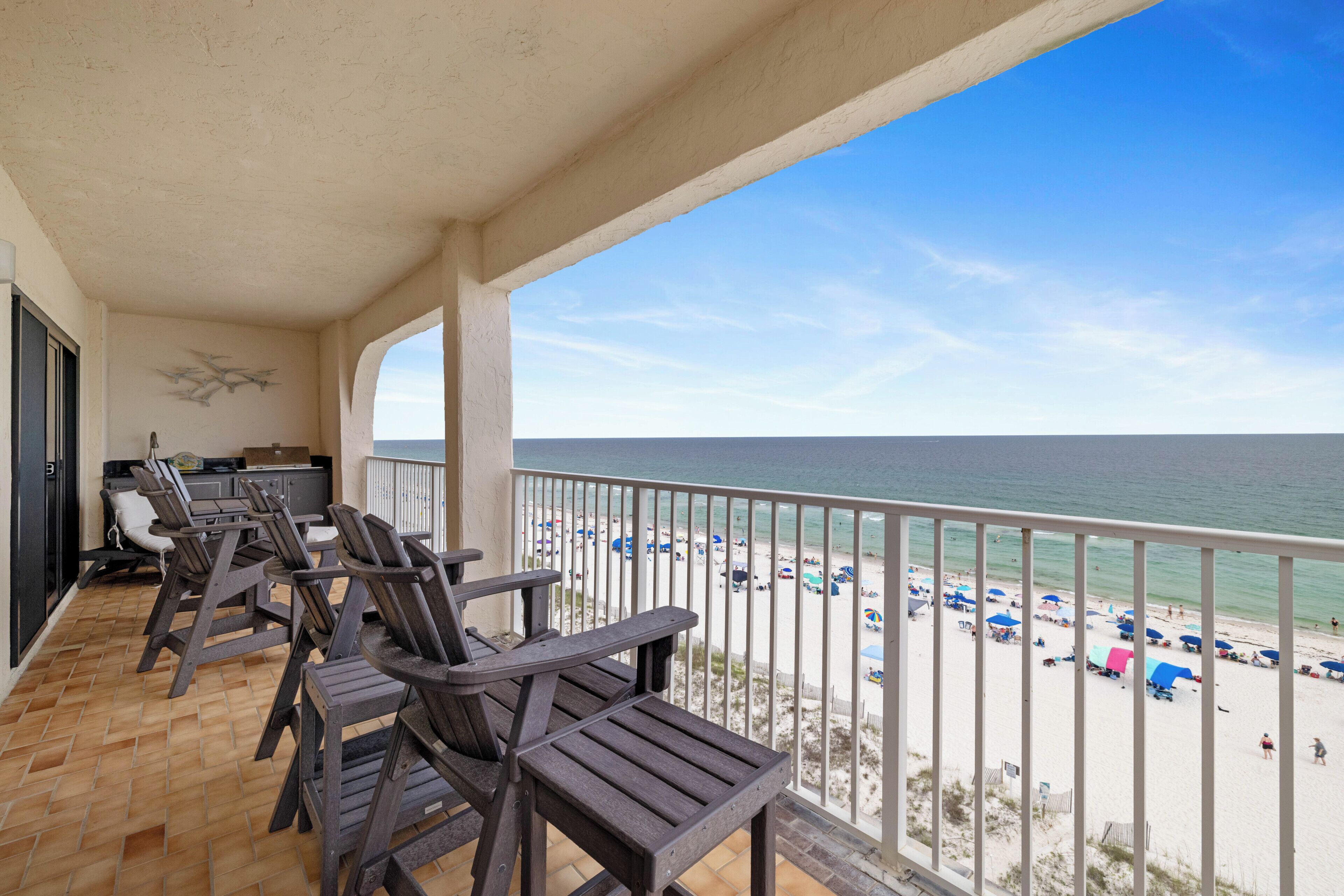 A balcony with wooden chairs, a small table, and a view of the beach.