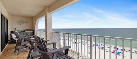 A balcony with wooden chairs, a small table, and a view of the beach.