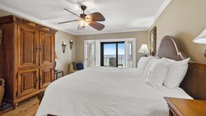 Une chambre avec un grand lit, un ventilateur de plafond, une armoire en bois et une vue sur l’extérieur.
