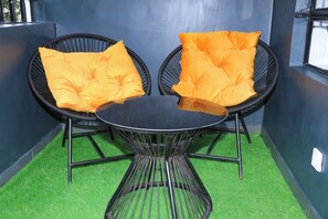 A room with a round table, two black wicker chairs, and bright orange cushions. - Rose Crown Suites (Nairobi)