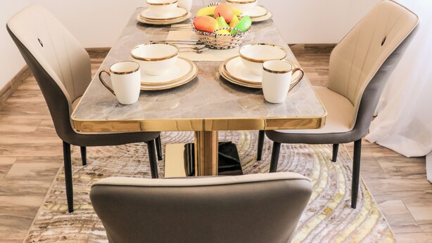 Una mesa de comedor con superficie de mármol, rodeada por cuatro sillas y una cesta de frutas en el centro.