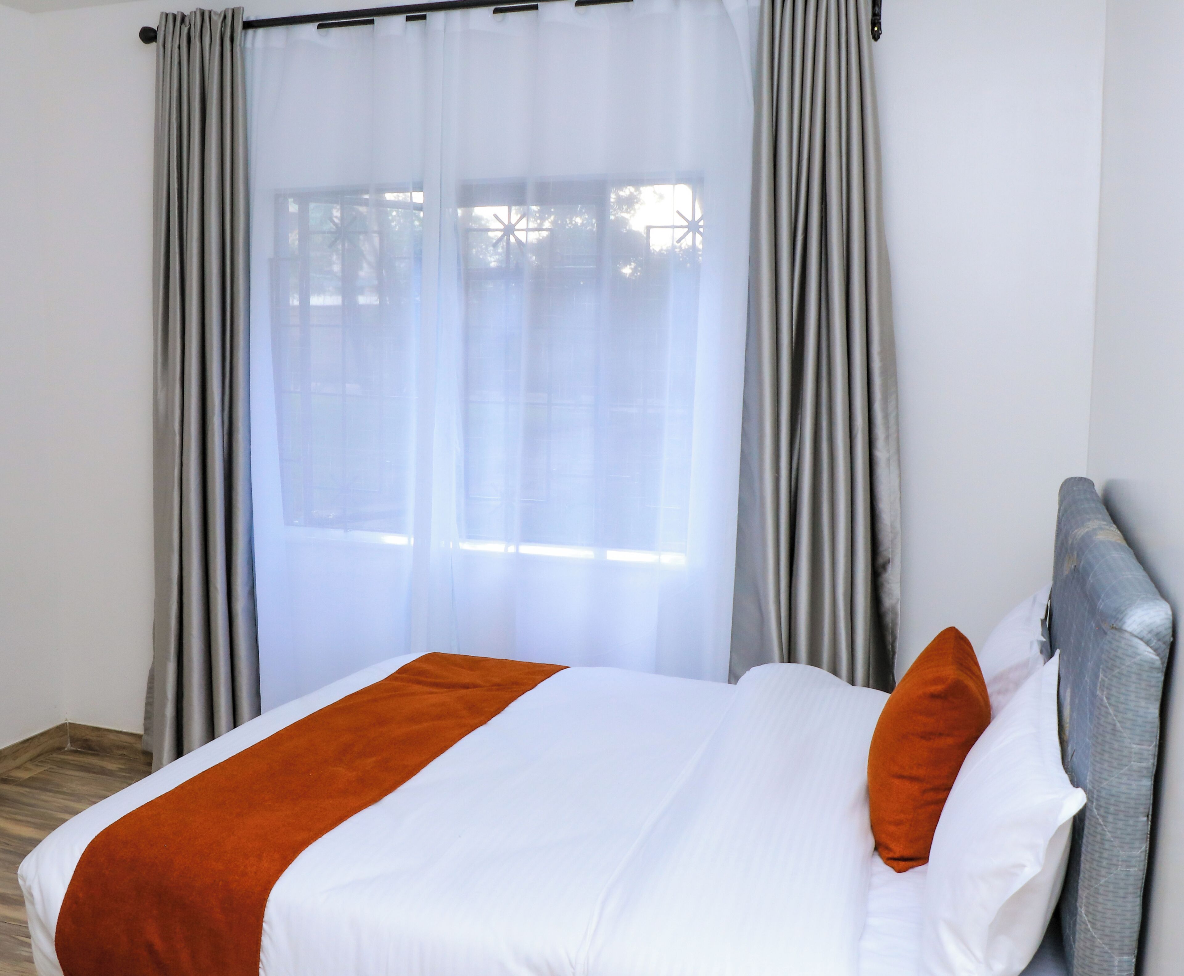 Una habitación de hotel con cama, cortinas grises y ventana.
