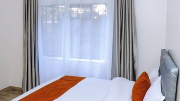 Una habitación de hotel con cama, cortinas grises y ventana.