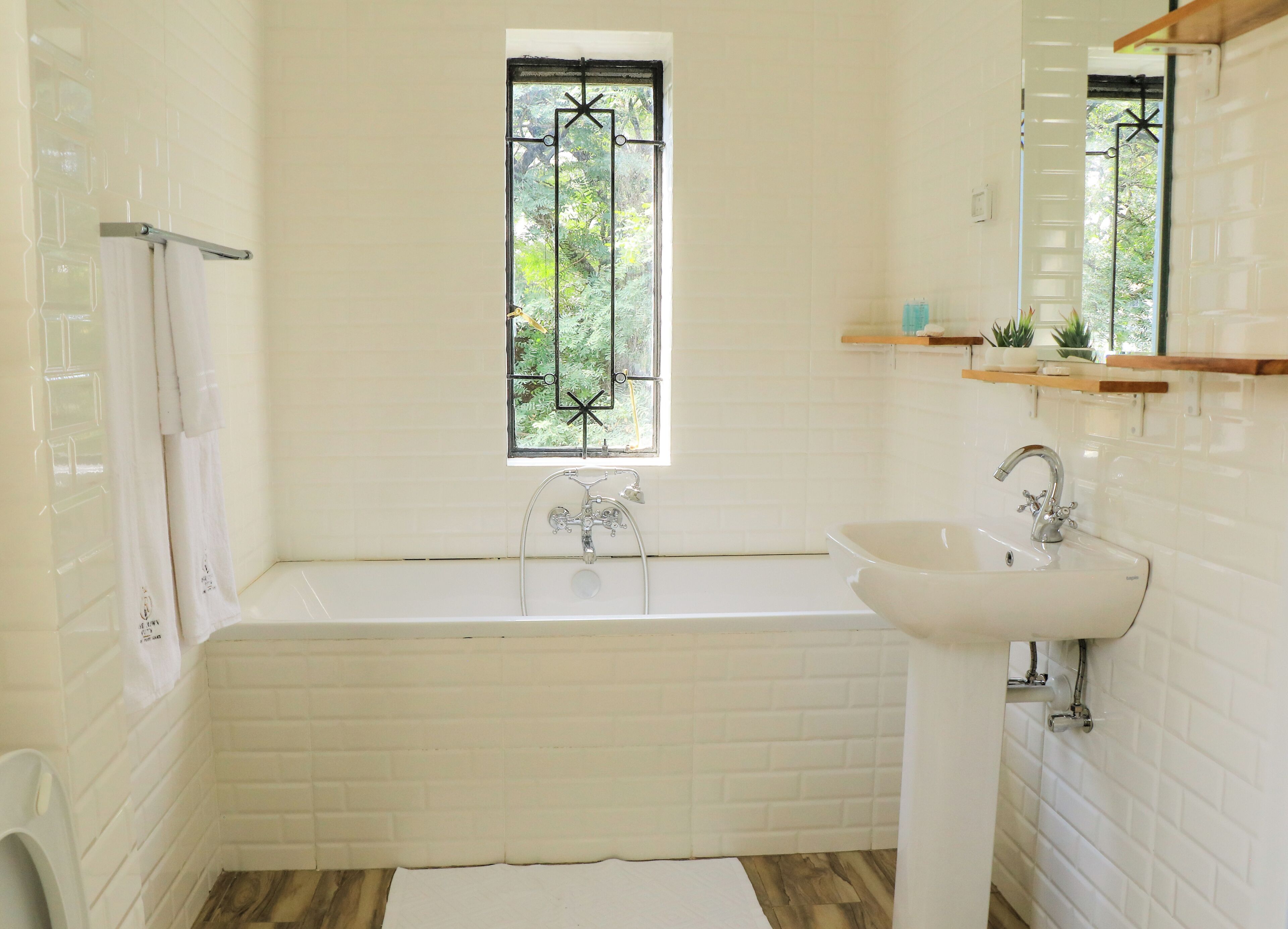 A bathroom with a white bathtub, a sink, a window with a view of greenery, and a towel rack.