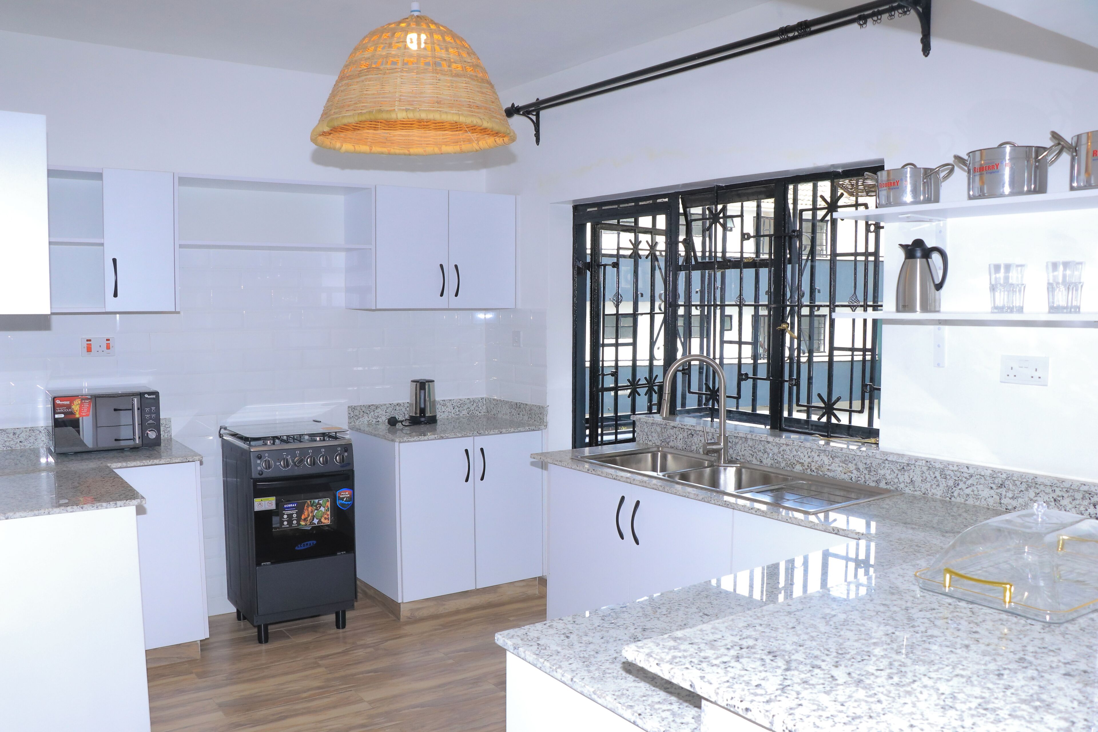 A kitchen with white cabinets, a microwave, a coffee machine, a sink, and a window with a metal gate.