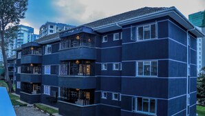 Un edificio residencial de varios pisos con balcones, ventanas grandes y un camino de entrada pavimentado.