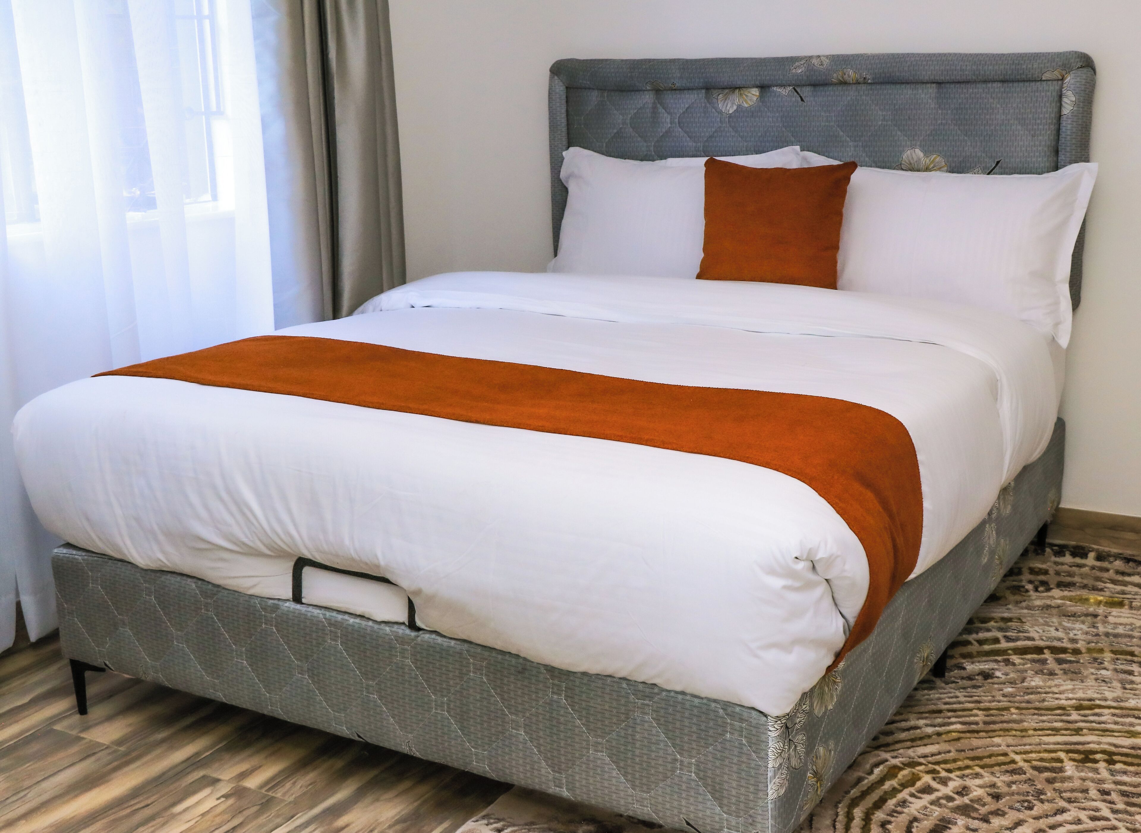 Ein Bett mit grauem Kopfteil, weißer Bettwäsche und braunen Akzenten.