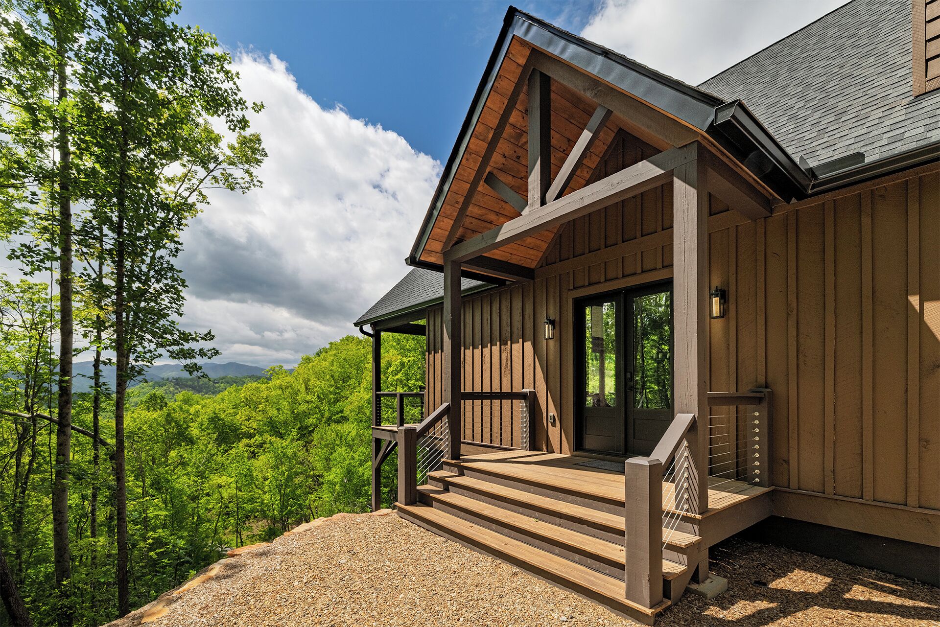A wooden cabin with a porch, a staircase, and a view of the forest.