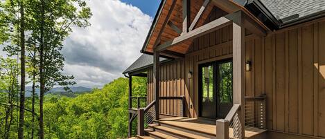 A wooden cabin with a porch, a staircase, and a view of the forest.