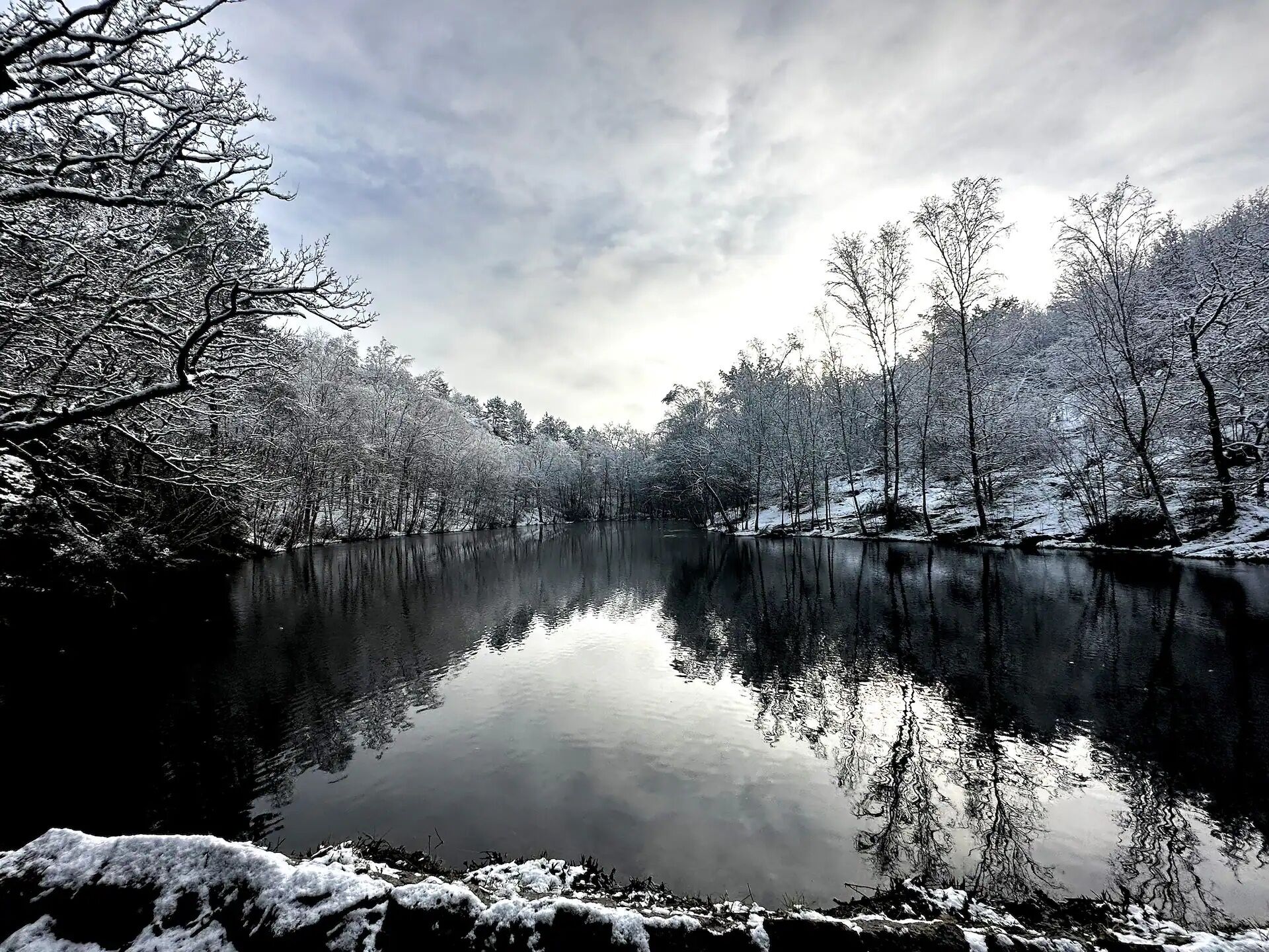 Ett stilla vinterlandskap med en lugn flod som speglar träd och himmel.