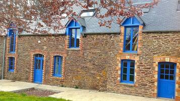 Un edificio de piedra con puertas y ventanas azules, techo inclinado y un pequeño jardín delantero.