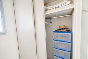 Ein Schrank mit Kleiderstange, einem blauen Aufbewahrungsbehälter und gefalteten Handtüchern auf der obersten Ablage.