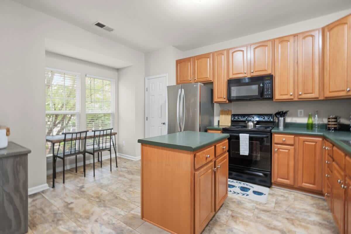 A kitchen with wooden cabinets, a stainless steel refrigerator, a microwave, and a stove.