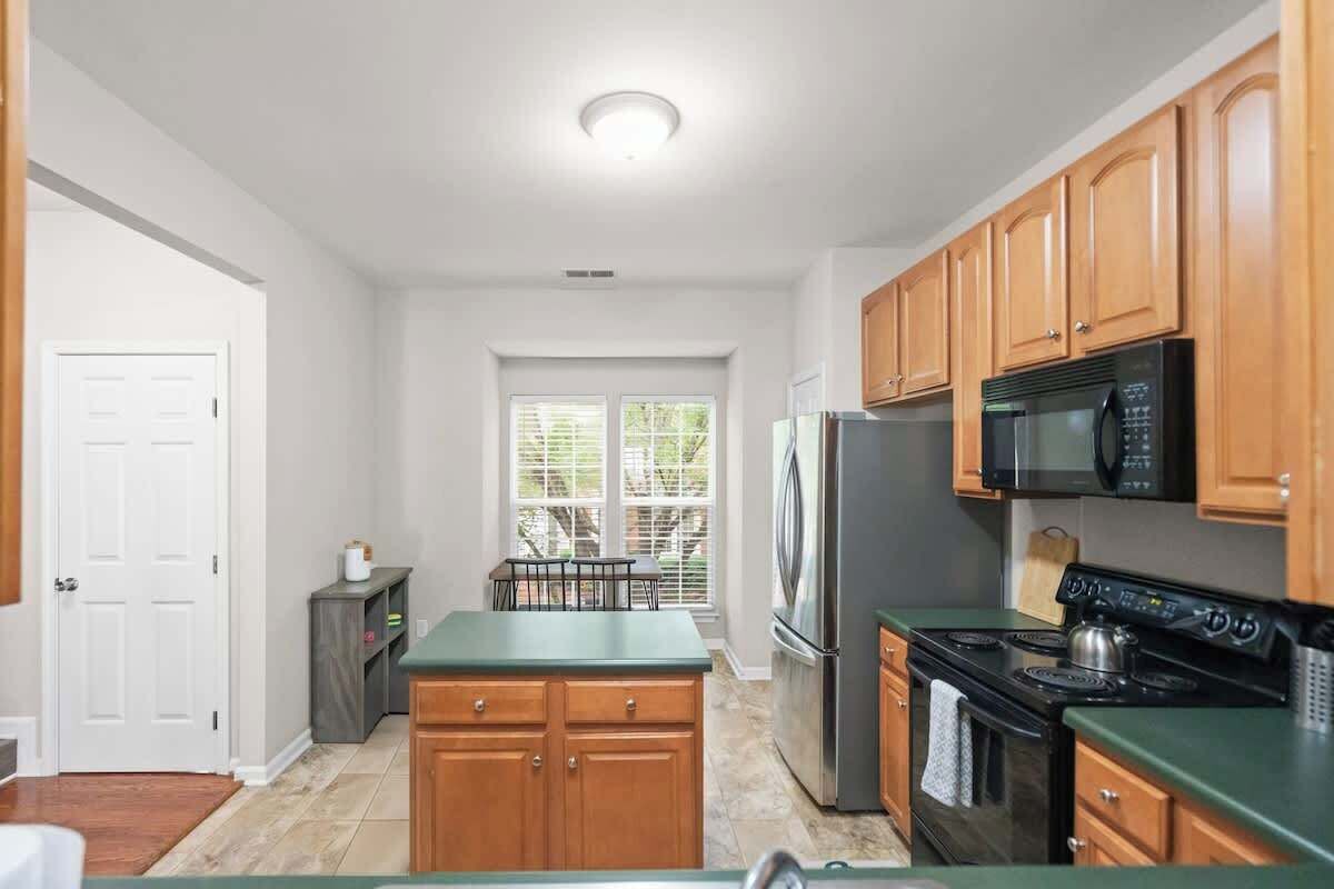 A kitchen with wooden cabinets, a refrigerator, a microwave, a stove, and a window with blinds.