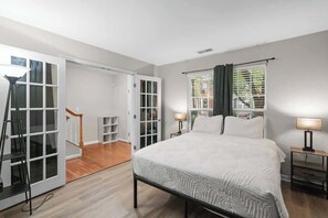 A bedroom with a bed, two bedside tables, a window with curtains, a door leading to a balcony, and a staircase. - Walking Distance to night life in Huntersville (Huntersville)