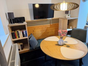 Ein modernes Zimmer mit einem Holz-Kopfteil, einem Flachbildfernseher, einem Bücherregal, einem runden Tisch mit Blumen in einer Vase und einem Sessel.