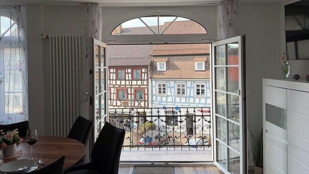 A dining area with a table, chairs, and a view of traditional buildings through an open door. - Old town view (Stockach)