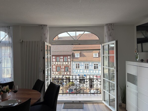 Ein Essbereich mit Tisch, Stühlen und Blick auf traditionelle Gebäude durch eine offene Tür.