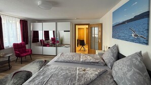 A modern hotel room with a bed, a seating area with a chair, a desk, and a large window. - Old town view (Stockach)