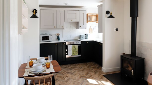 Una cucina moderna con stufa a legna, mobili bianchi e zona pranzo con tavolo apparecchiato per quattro.
