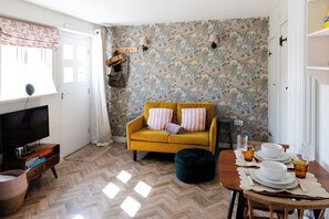 Ein Wohnzimmer mit einer Couch, einem Fernseher und einem Esstisch, gedeckt mit Tellern und Gläsern.