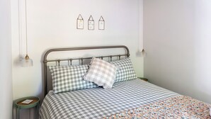 Un letto ben rifatto con lenzuola a quadri, un comodino con una lampada e un'opera d'arte appesa alla parete.