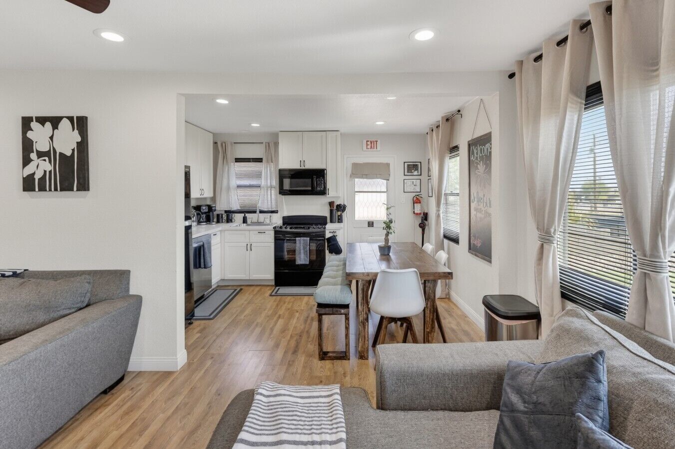 Una cucina moderna con mobili bianchi, un piano cottura nero e una zona pranzo con tavolo e sedie in legno.
