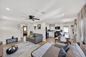 A modern living room with a sofa, ottoman, and a dining area with a table and chairs.