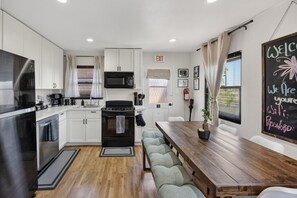 A modern kitchen with white cabinets, a black stove, and a wooden dining table with benches.