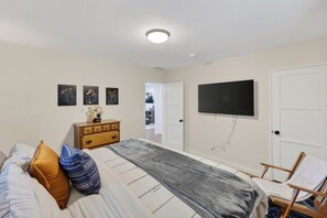 A bedroom with a bed, a dresser, a chair, a television, and a door.