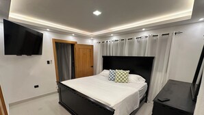 Ein modernes Schlafzimmer mit einem Bett, einem an der Wand befestigten Fernseher, einem Kleiderschrank und einem kleinen Tisch.