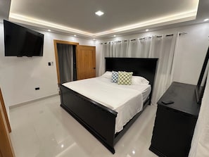 Ein modernes Schlafzimmer mit einem Bett, einem an der Wand befestigten Fernseher, einem Kleiderschrank und einem kleinen Tisch.