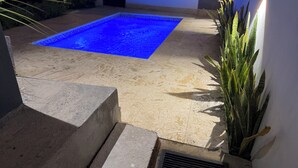 Ein Pool mit blauer Färbung, umgeben von einer Betonplattform und Topfpflanzen.